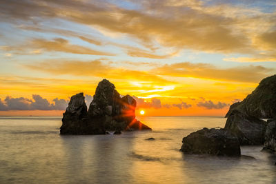 Rock formation in sea against sky during sunset