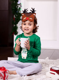 Portrait of cute girl holding mug sitting on bed at home