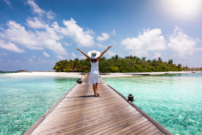 Rear view of woman with arms raised on jetty over sea against sky