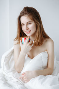 Portrait of young woman holding mug while sitting on bed