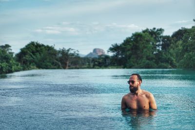 Shirtless man swimming in lake against sky