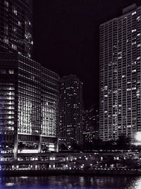 Illuminated building by river against sky at night