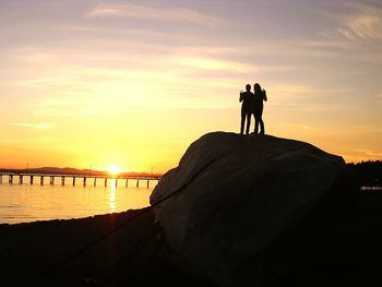 Silhouette women standing on rock at beach against sky during sunset