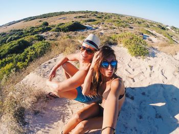 Fish-eye view of couple sitting on sand against sky