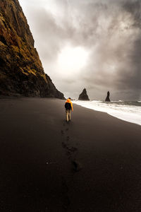 Rear view of man walking at beach against sky