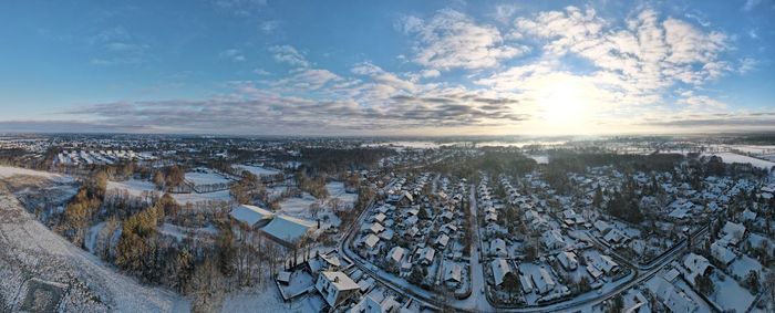 Scenic view of frozen river by buildings against sky during sunset