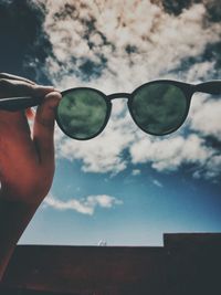 Close-up of hand holding sunglasses against sky