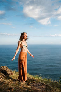 Young woman standing on cliffs edge with closed eyes near ocean. tranquility and mndfulness concept.