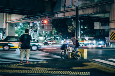 Rear view of people and vehicles on city street at night