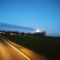 Road amidst field against clear blue sky at night
