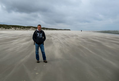 Full length portrait of man standing at beach against sky
