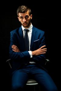 Portrait of businessman sitting on chair against black background