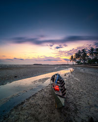 Motor scooter on beach against sky during sunset