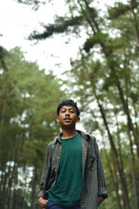 Low angle view of young man looking away against trees