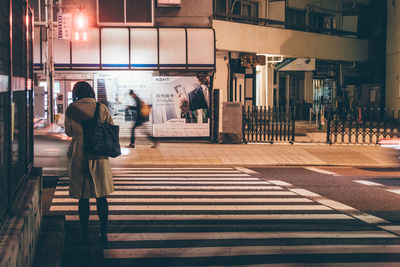 Rear view of woman walking on zebra crossing at night