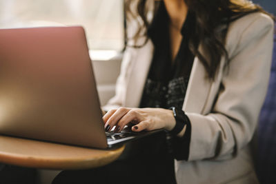 Midsection of businesswoman using laptop while commuting in train