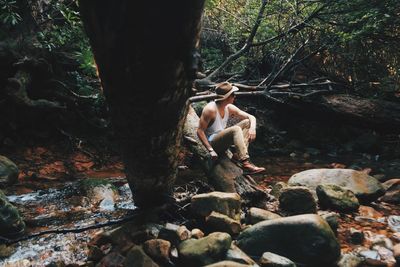 Man sitting on fallen tree over stream in forest