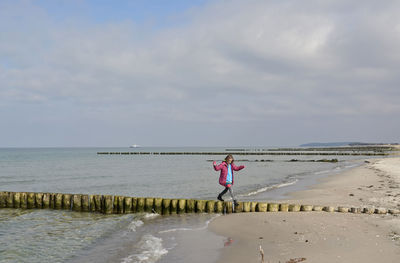 Full length of woman walking on wooden post at beach against sky
