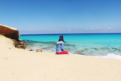 Woman sitting at beach against blue sky