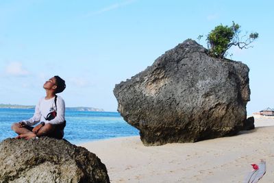 Man sitting on rock by sea against sky