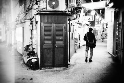 Rear view of man walking on street amidst buildings