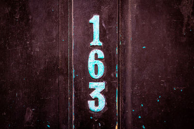 House number 163 vertically aligned on a black wooden front door in london 