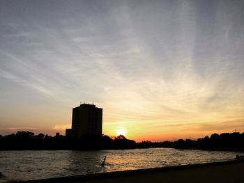 Silhouette city by sea against sky during sunset