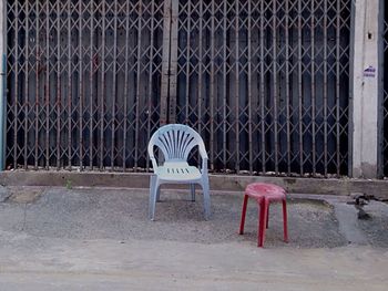 Empty chairs on metal fence against abandoned building