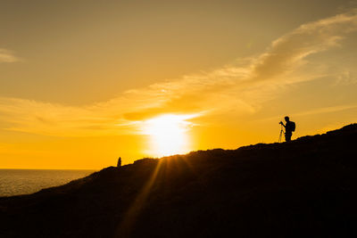 Silhouette people standing on land against sky during sunset