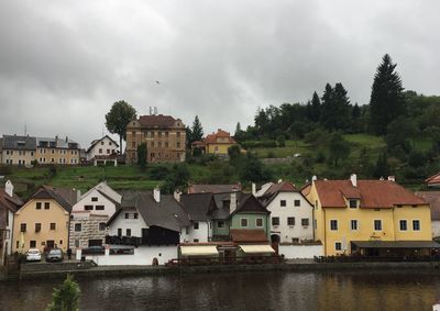 Houses by river against buildings in city against sky