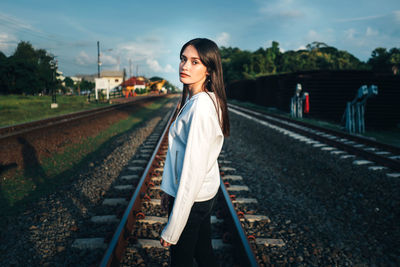 Portrait of woman standing on railroad track against sky
