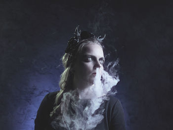 Spooky young woman emitting smoke from nose against black background