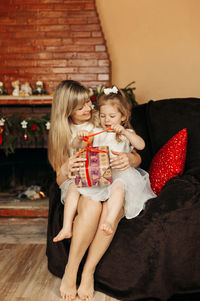 A happy mother and a girl with a gift box on the background of the fireplace.