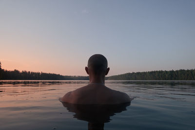 A man swims in a forest lake in the evening. back view. alone with nature.