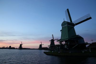 Traditional windmills by sea against sky during sunset