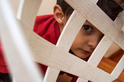 Portrait of cute boy looking through wooden railing