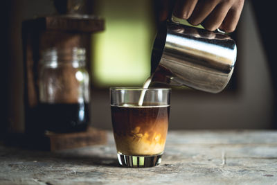 Cropped hand pouring milk in coffee on table