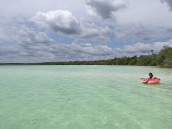 Young woman sitting on sea against sky