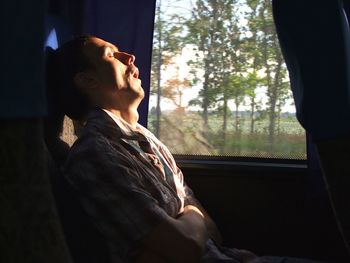 Side vie of man sleeping while sitting by window in train