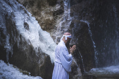 Side view of man standing on rock against waterfall
