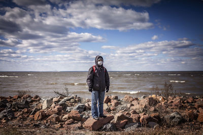 Full length of man standing on rock at beach against sky