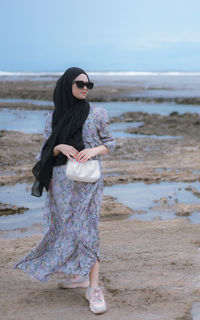 Young woman standing at beach against sky