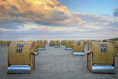 Hooded chairs on beach against sky during sunset