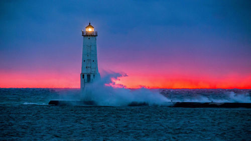 Lighthouse by sea against sky during sunset