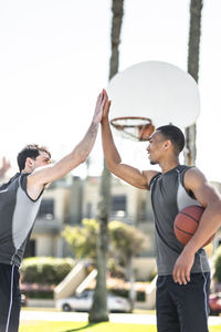 Two young men high-fiving on outdoor basketball court