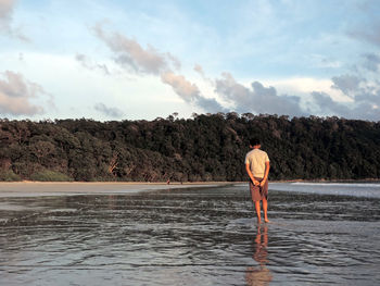 Rear view of man standing on shore at beach against sky