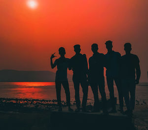 Silhouette people on beach against orange sky