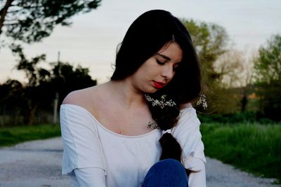 Young woman wearing off shoulder sitting against sky during sunset