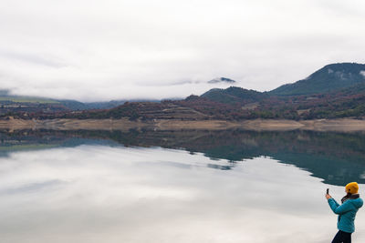 Rear view of woman standing by lake against sky