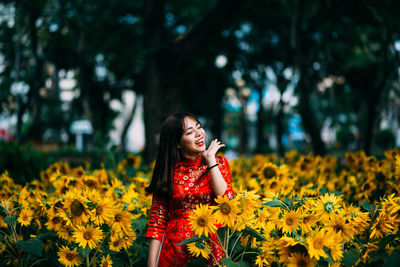 Happy young woman standing amidst yellow flowers